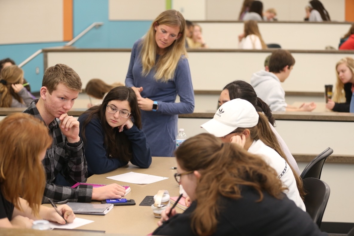 Professor stands among students in classroom.