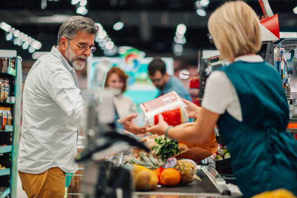 Customer unloading groceries at checkout with cashier