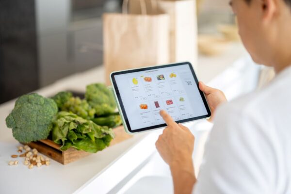 Man ordering groceries on a tablet while in a kitchen with vegetables on counter