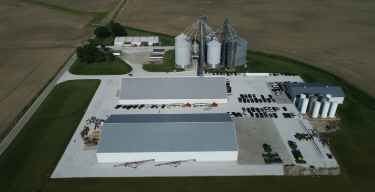 Aerial view of large commercial farm site with multiple sheds, farm office, grain bins, and house