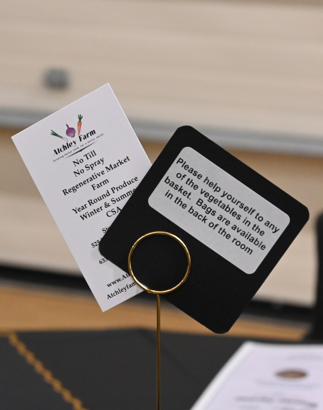 Gold clip holding an Atchley Farm business card and a sign inviting visitors to help themselves to vegetables