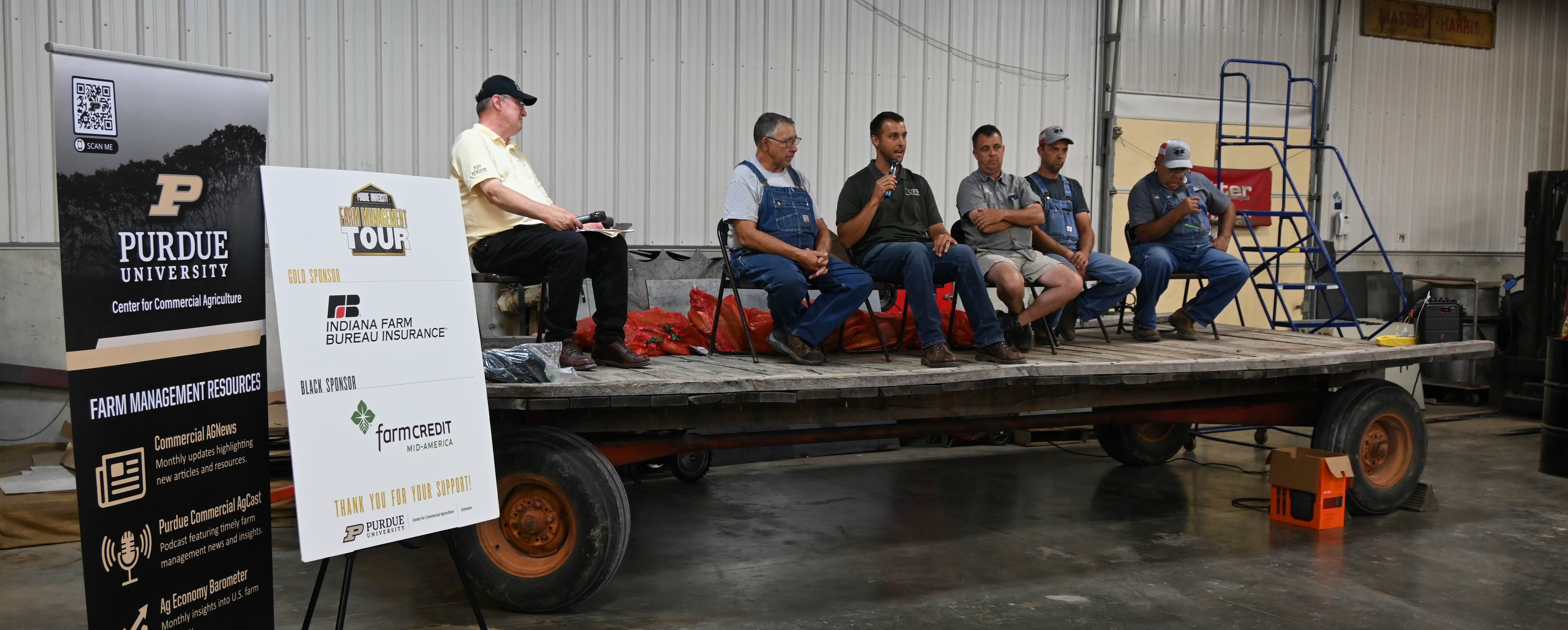 Two Purdue posters on the left side of a flatbed trailer with a group of panelists on top
