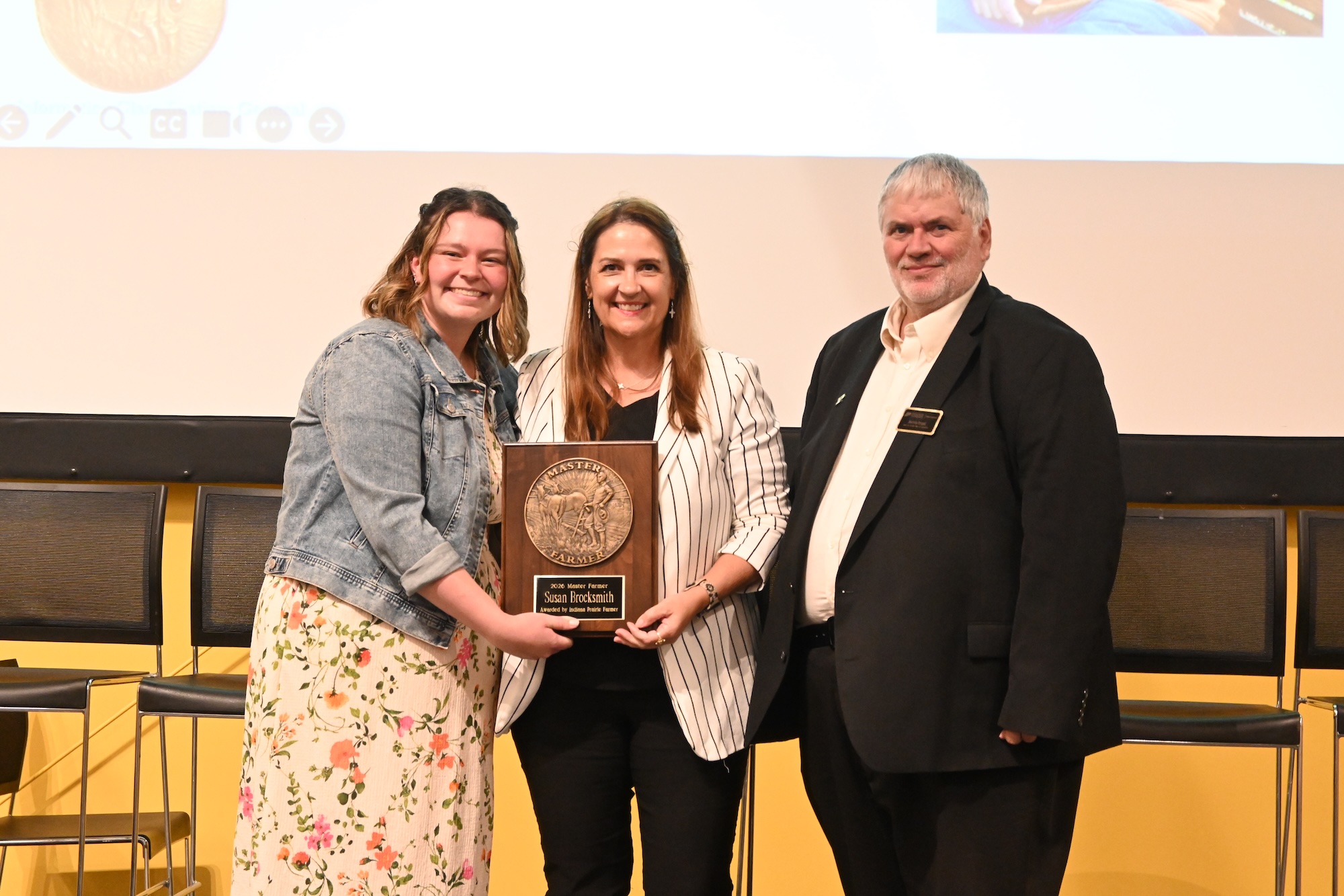 Allison Lynch and Dean Engel standing with Susan Brocksmith holding her Master Farmer award