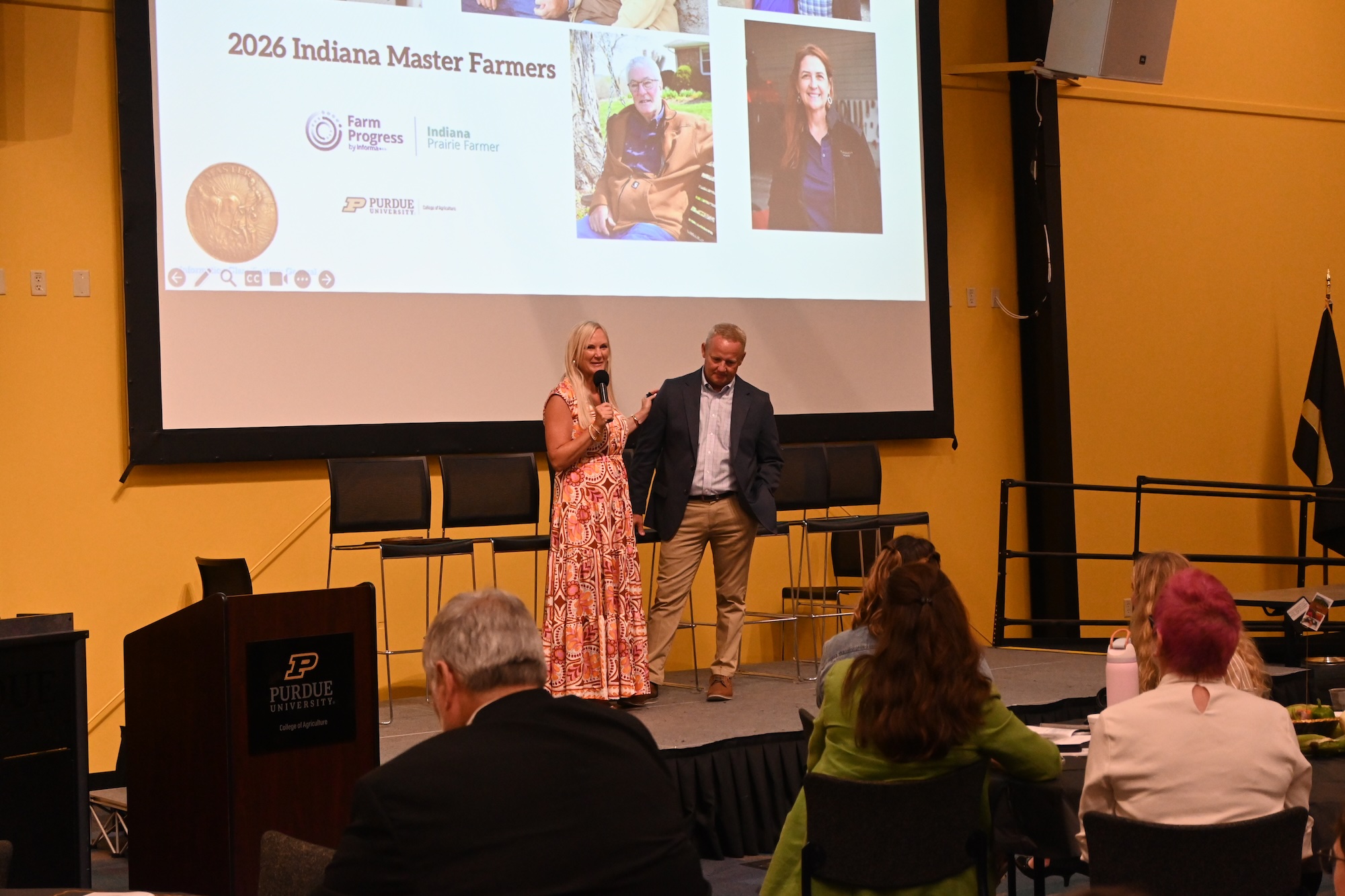 Dale and Lisa Koester speaking on stage in front of Master Farmer ceremony attendees