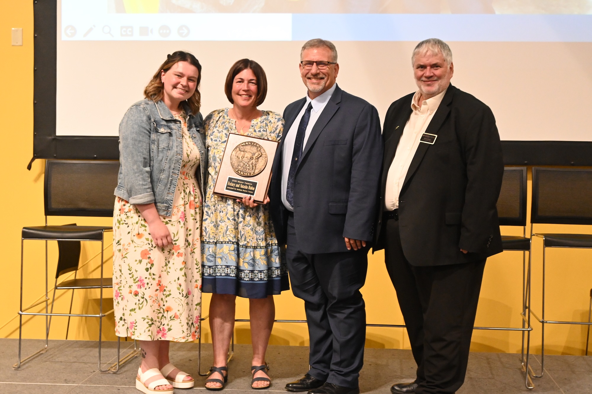  Allison Lynch and Dean Engel standing with Rodney and Natasha Rulon holding their Master Farmer award