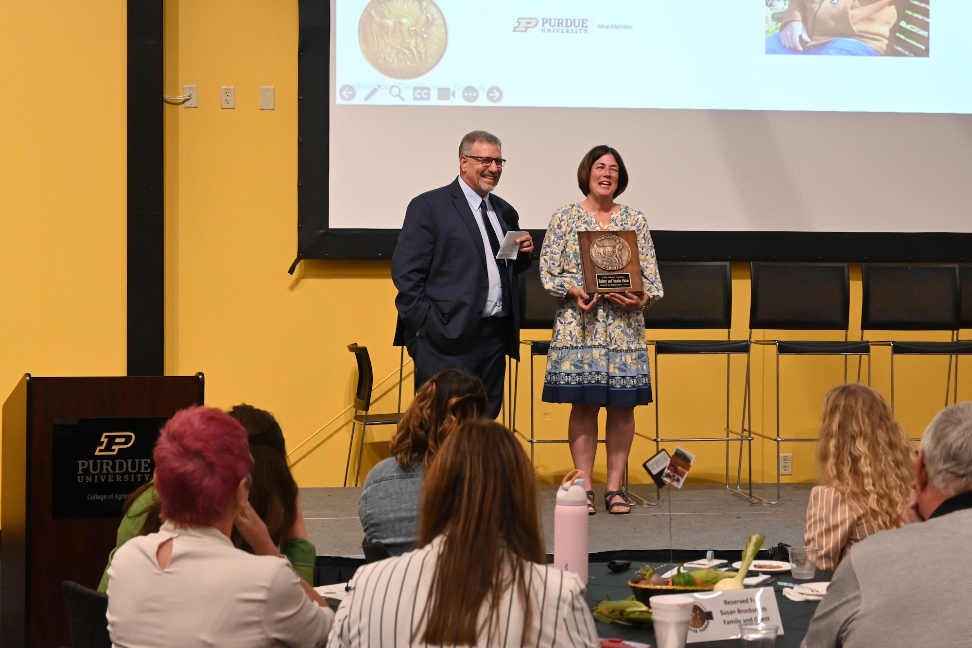 Rodney and Natasha Rulon speaking on stage in front of Master Farmer ceremony attendees