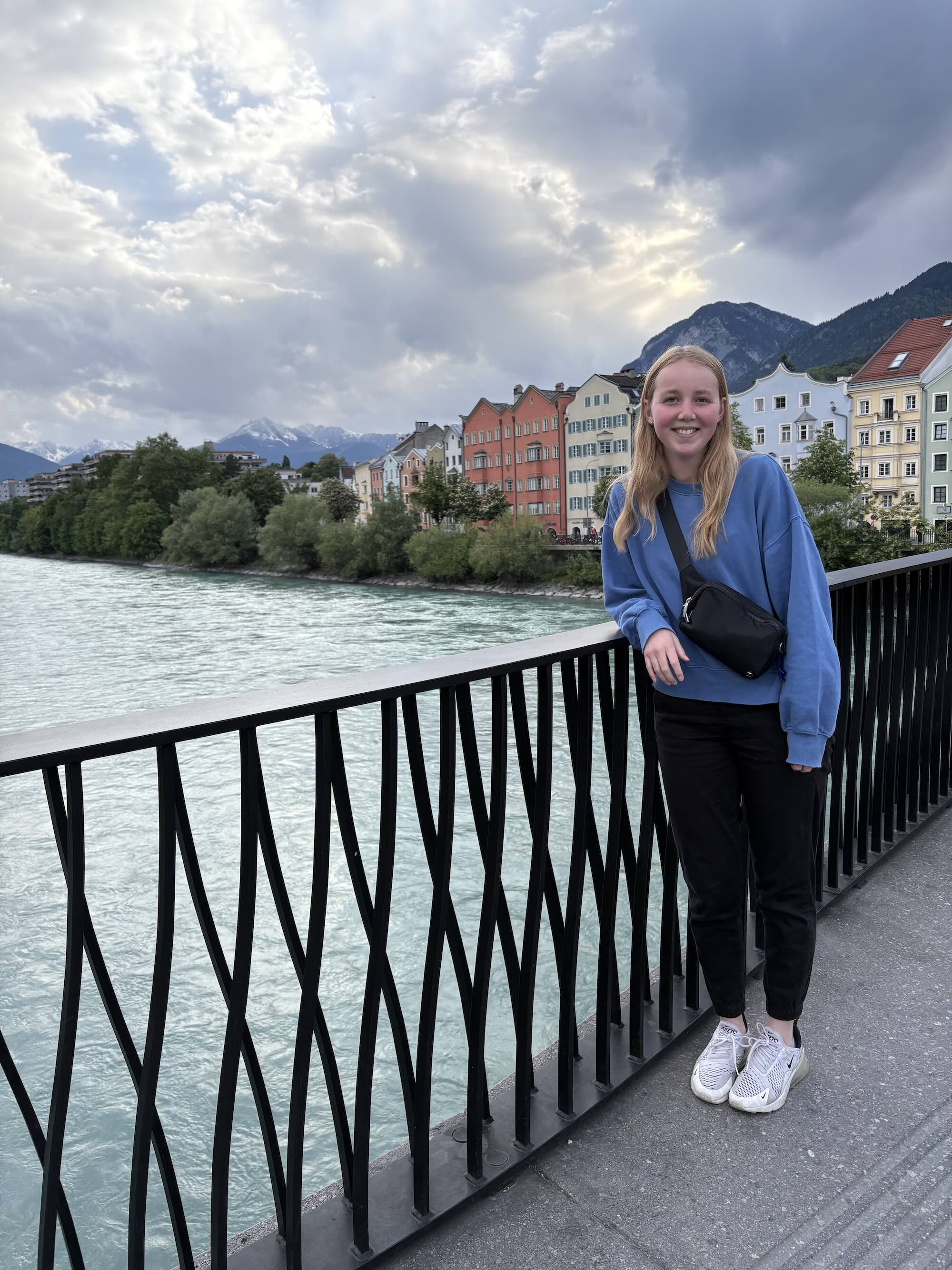 Baker standing on a bridge overlooking a blue river in an abroad trip