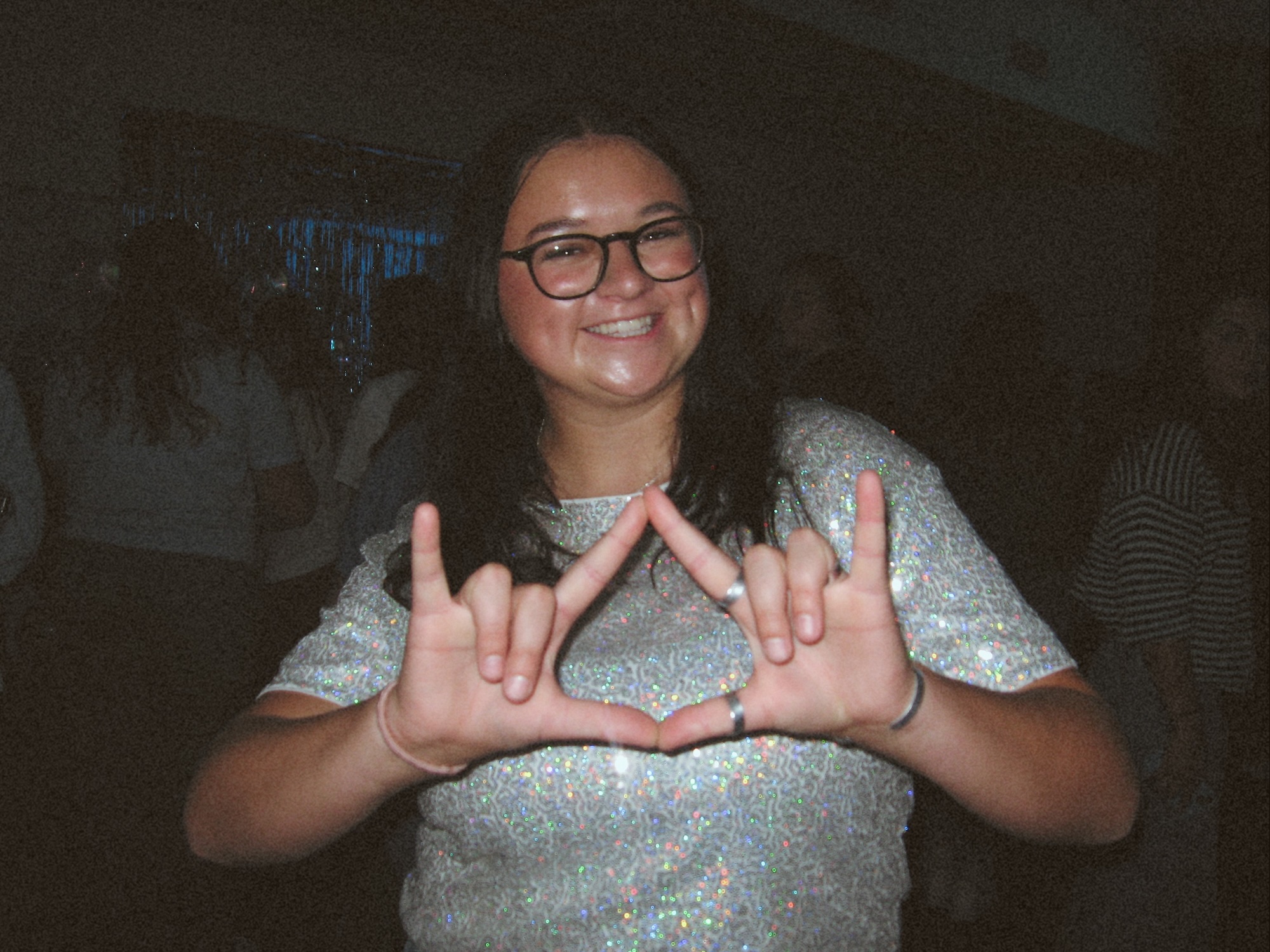 Blacker in a white sequin shirt throwing a sorority sign