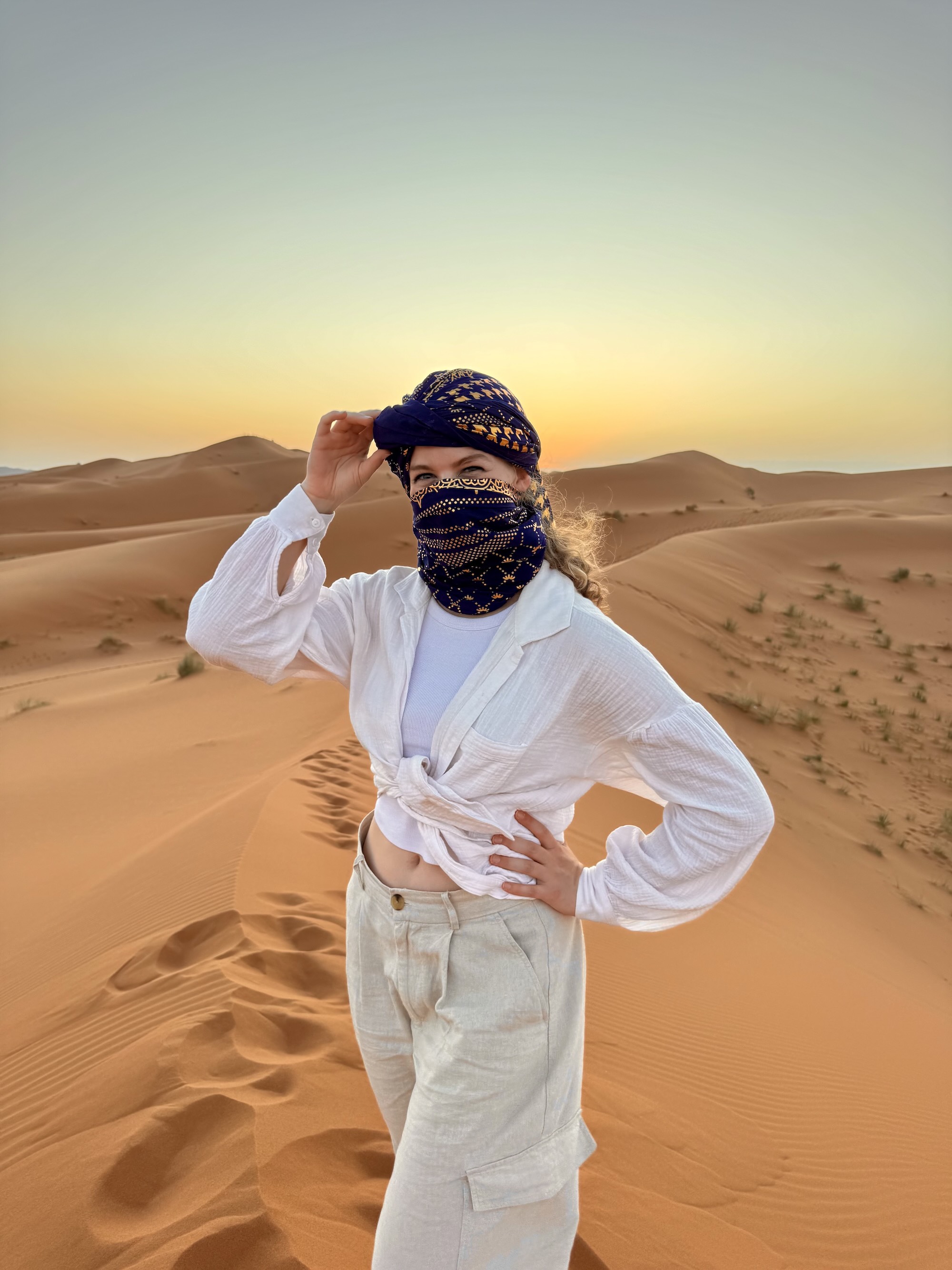 Clary standing in a desert under a dark blue hood and scarf