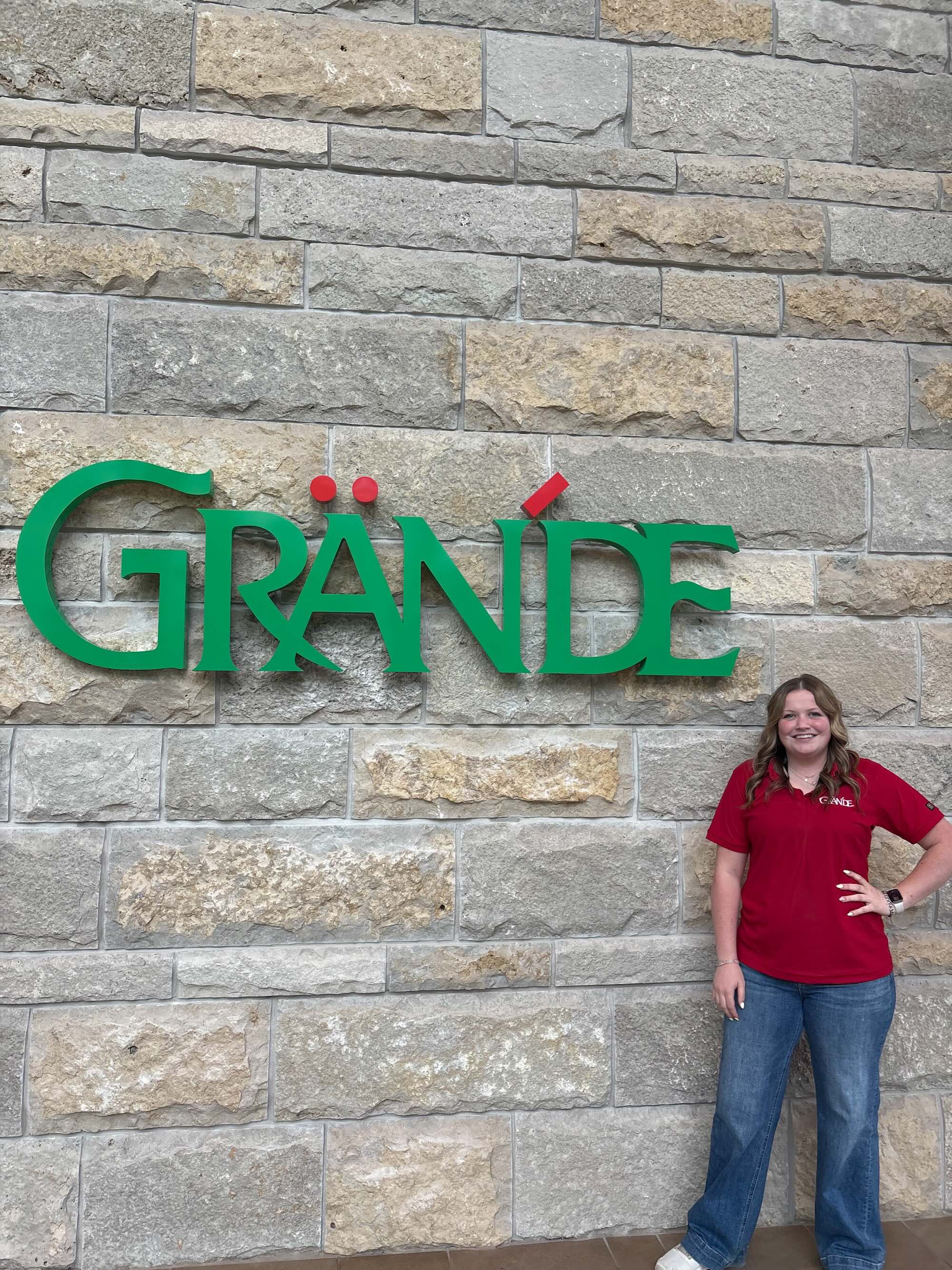 Cooper standing in front of a Grande business sign on a brick wall