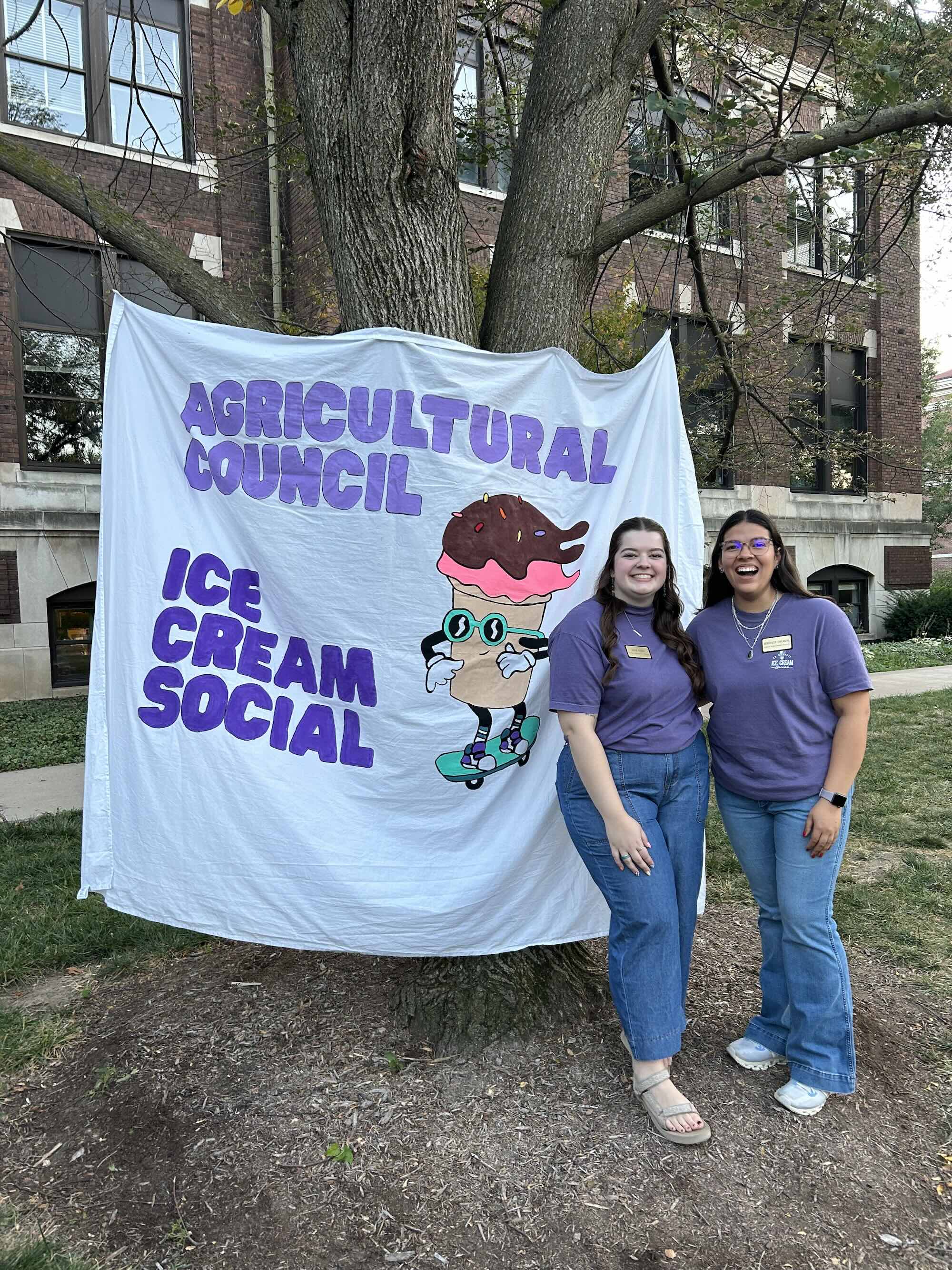 Berenize standing with a friend in front of the ag council ice cream social banner