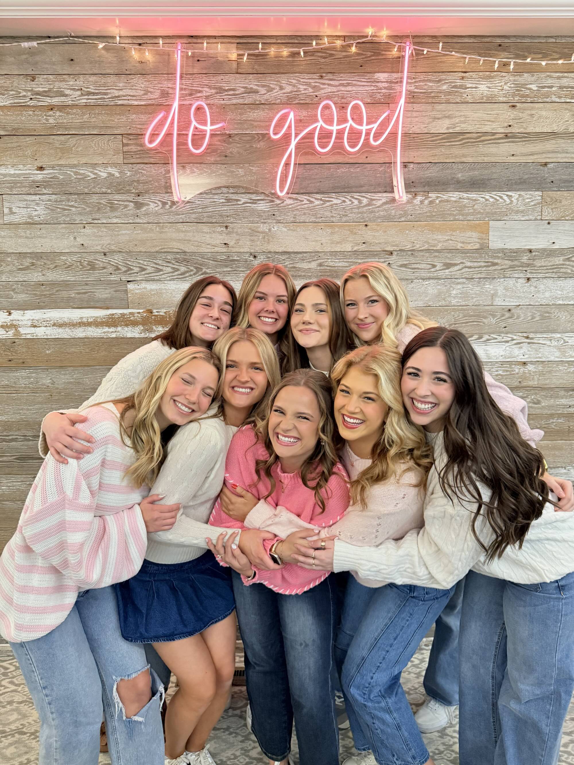 Kelsay with friends in front of pink neon do good sign