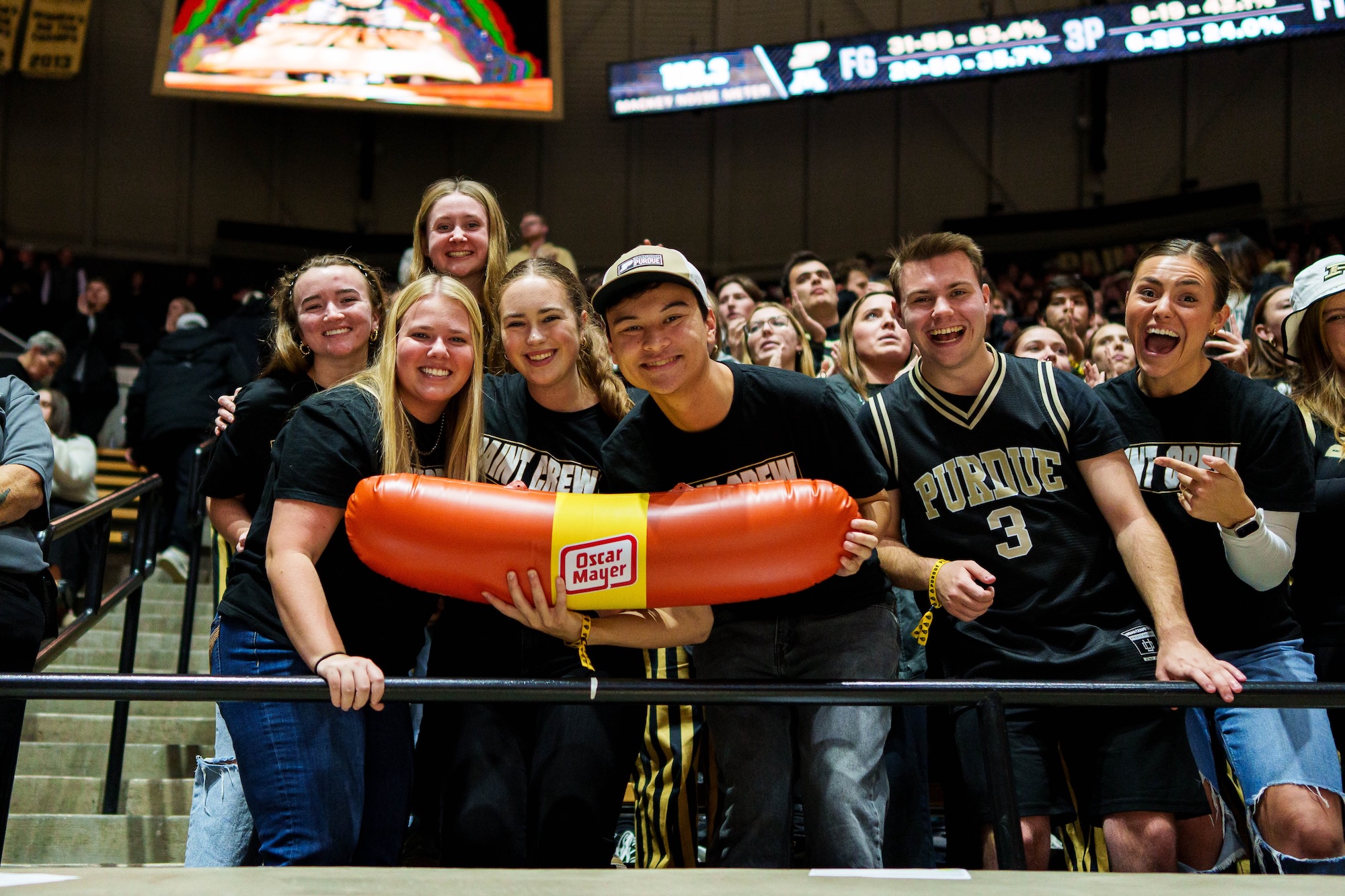 Logue with friends at a basketball game and holding a giant Oscar Mayer hotdog