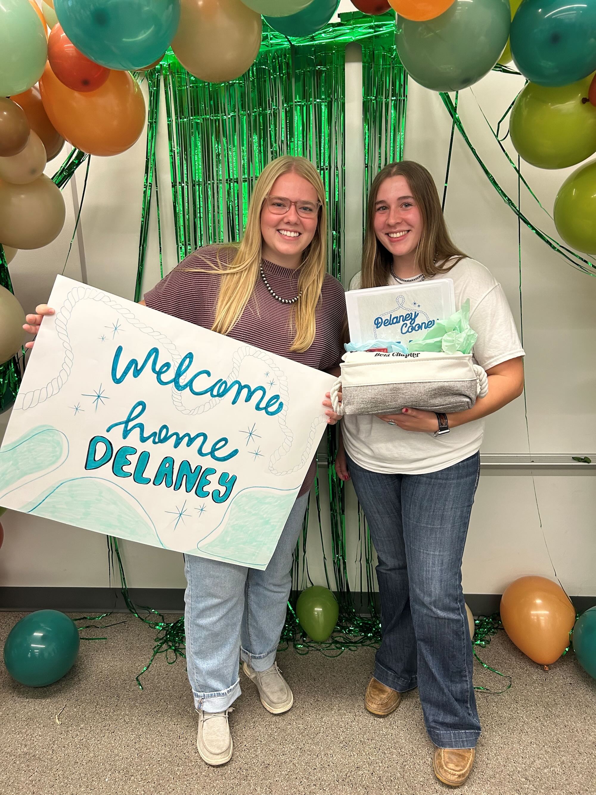 Logue holding a welcome home sign and standing next to her sorority little