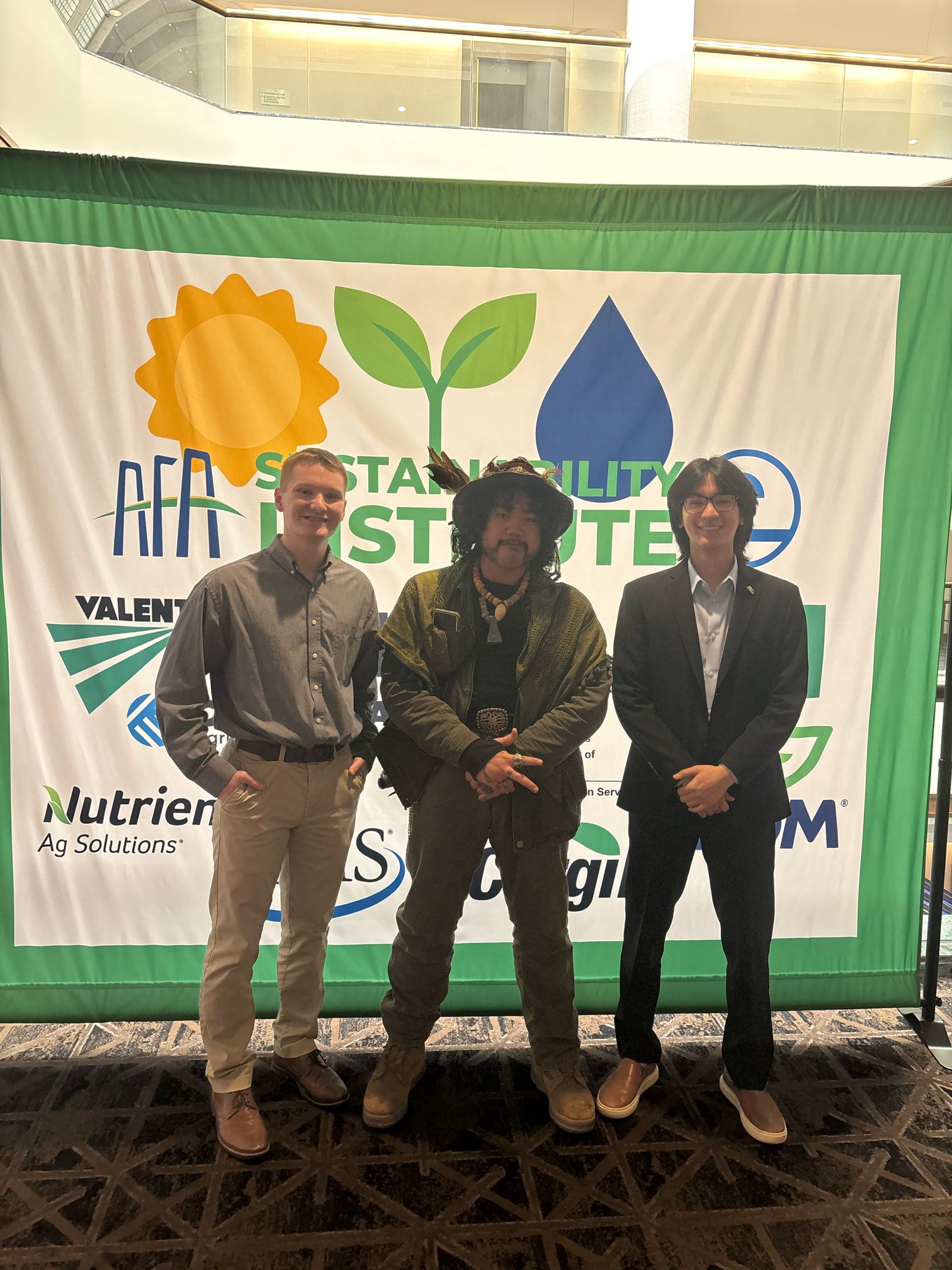 Kenny Yamauchi standing with friends in front of AFA sustainability banner