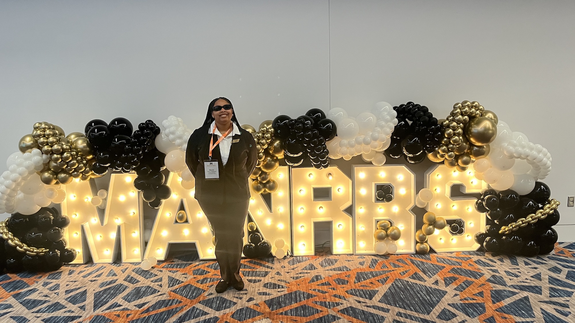 Brynn standing in front of the MANRRS sign lit up with Purdue brand balloons