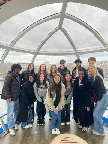 Abroad group smiling together inside a glass London Eye observation pod overlooking a river and city skyline.