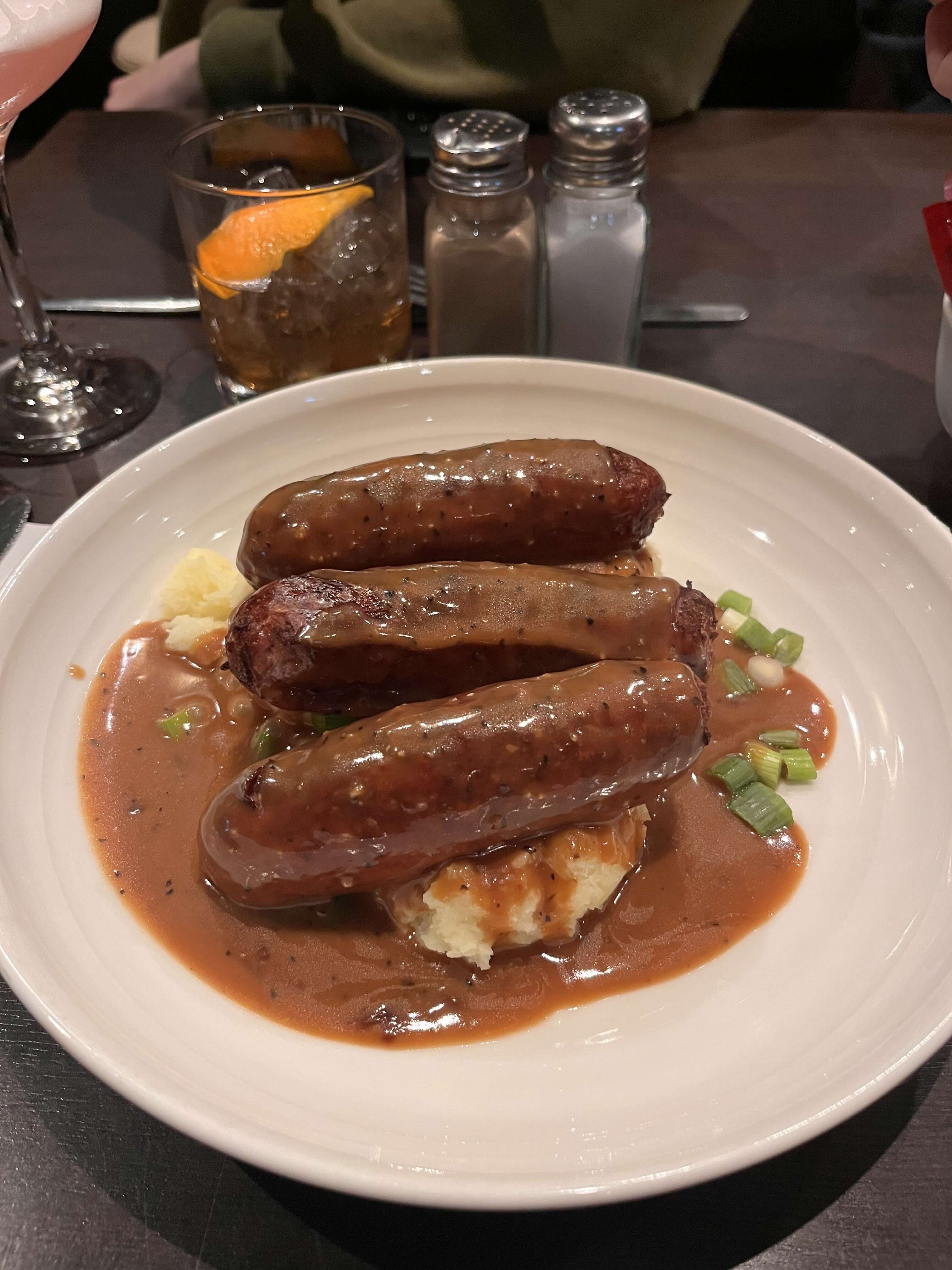 Bangers and mash on a plate; salt and pepper shakers, and a cocktail with an orange peel.