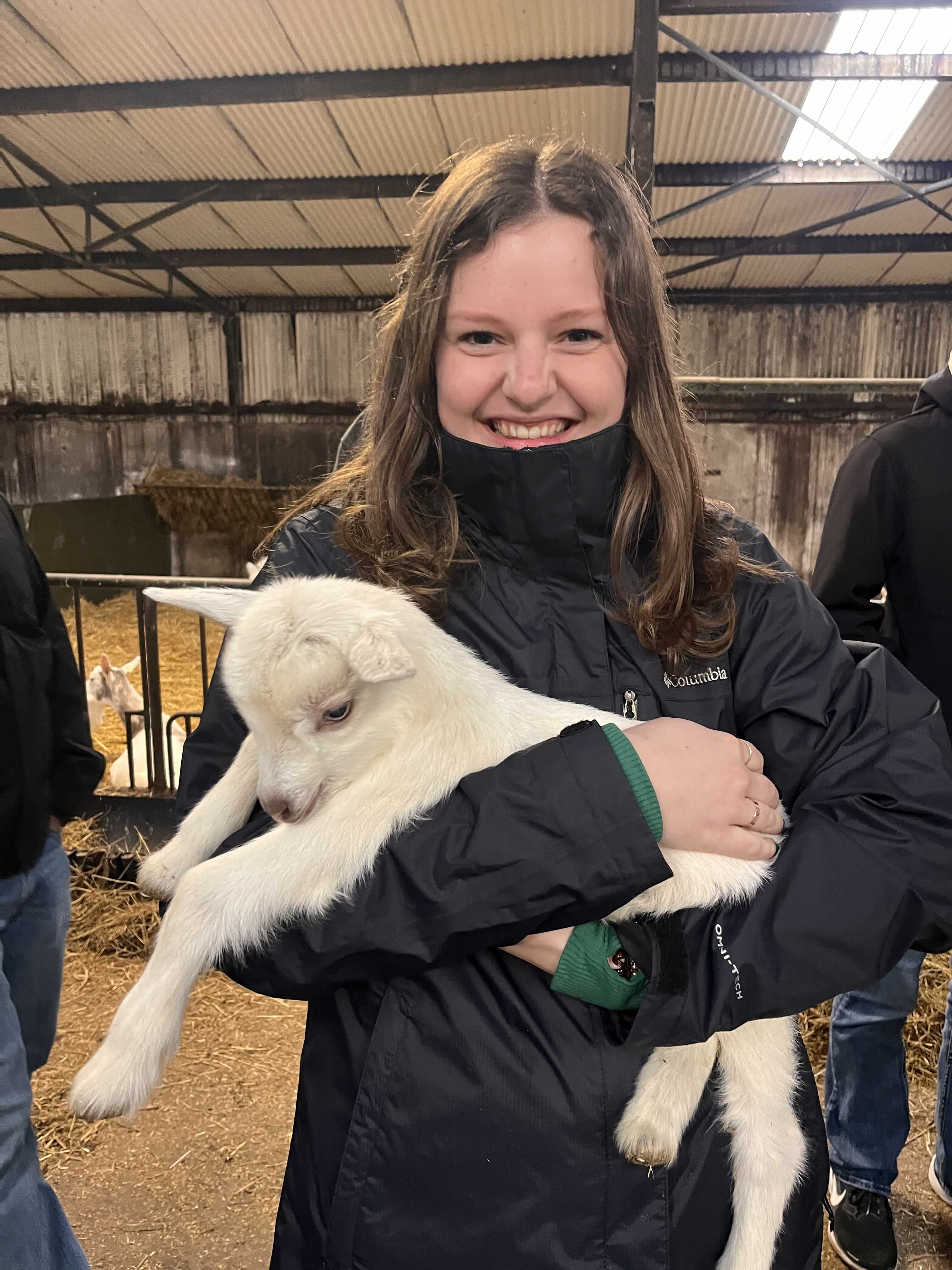 Jade Larrison holding a white baby goat inside a barn