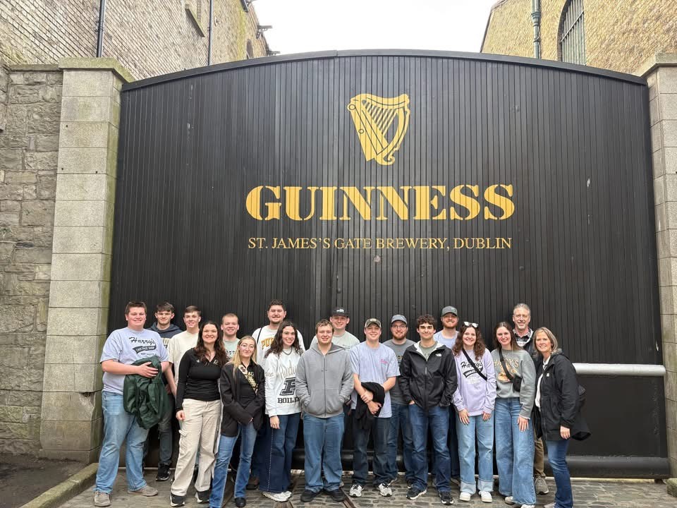 Study abroad group posing in front of a large black gate bearing the GUINNESS logo at St. James’s Gate Brewery in Dublin.