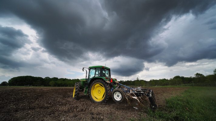 tractor and plow in a field with stormy skies above