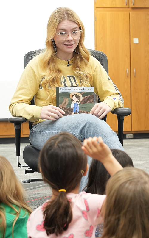 Purdue student reading a book to a group of young children