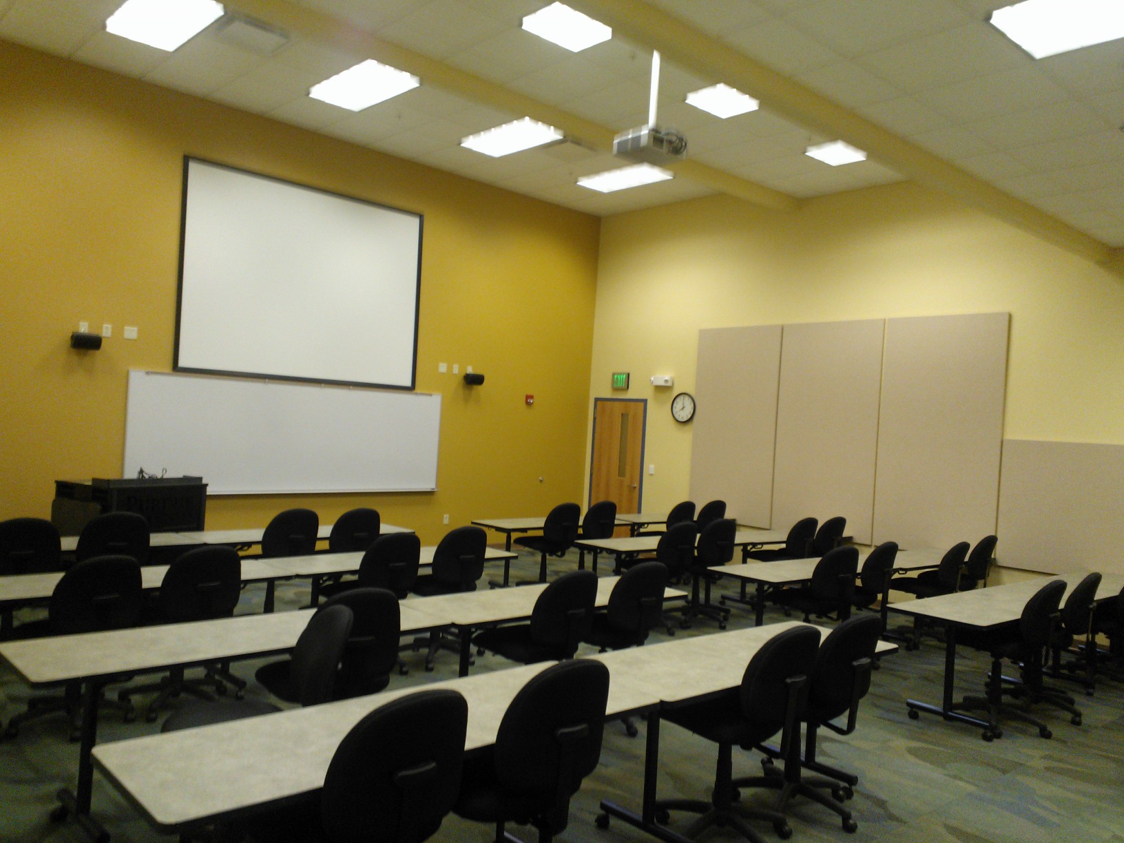 Room 141 set up in classroom style seating for 36 guests. Chairs are cushioned and on wheels. Big screen and white board on the wall for presentations.