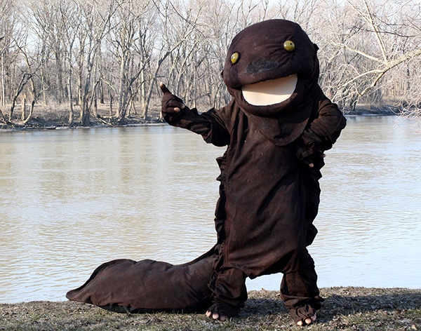 Herbie the Hellbender mascot standing with river in the background.