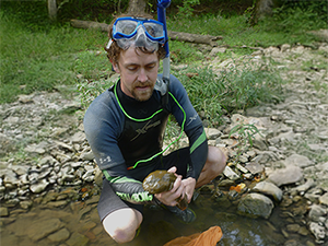 Staff holding hellbender in river.
