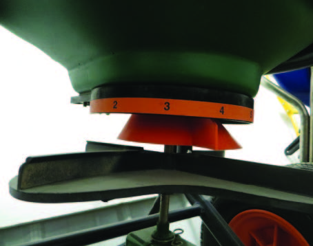 This spreader uses a rotating conical distribution device to adjust where the fertilizer hits the impeller, which adjusts the spread pattern.