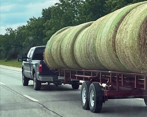 The hay may look secure, there is nothing holding the hay down except gravity. A sharp turn could cause the bales to roll onto the roadway.