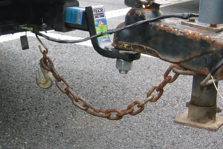 This trailer has only one chain attached when it should have two. In addition, the chain is hooked on by a link instead of the hook that is provided. Use hooks that fit the attachment points on the towing truck, and that match the chain’s breaking strength.
