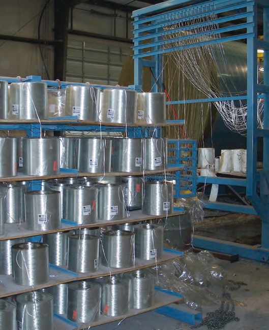 Next to the mold, spools of glass strand are lined up on racks.