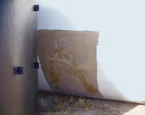This storage tank was not anchored and blew over when a storm passed through. The fiberglass tank struck the concrete containment wall, which produced a 4-foot long crack. In the brown sanded and fiberglassed area, the lighter colored crack has been repaired, but can still be seen.