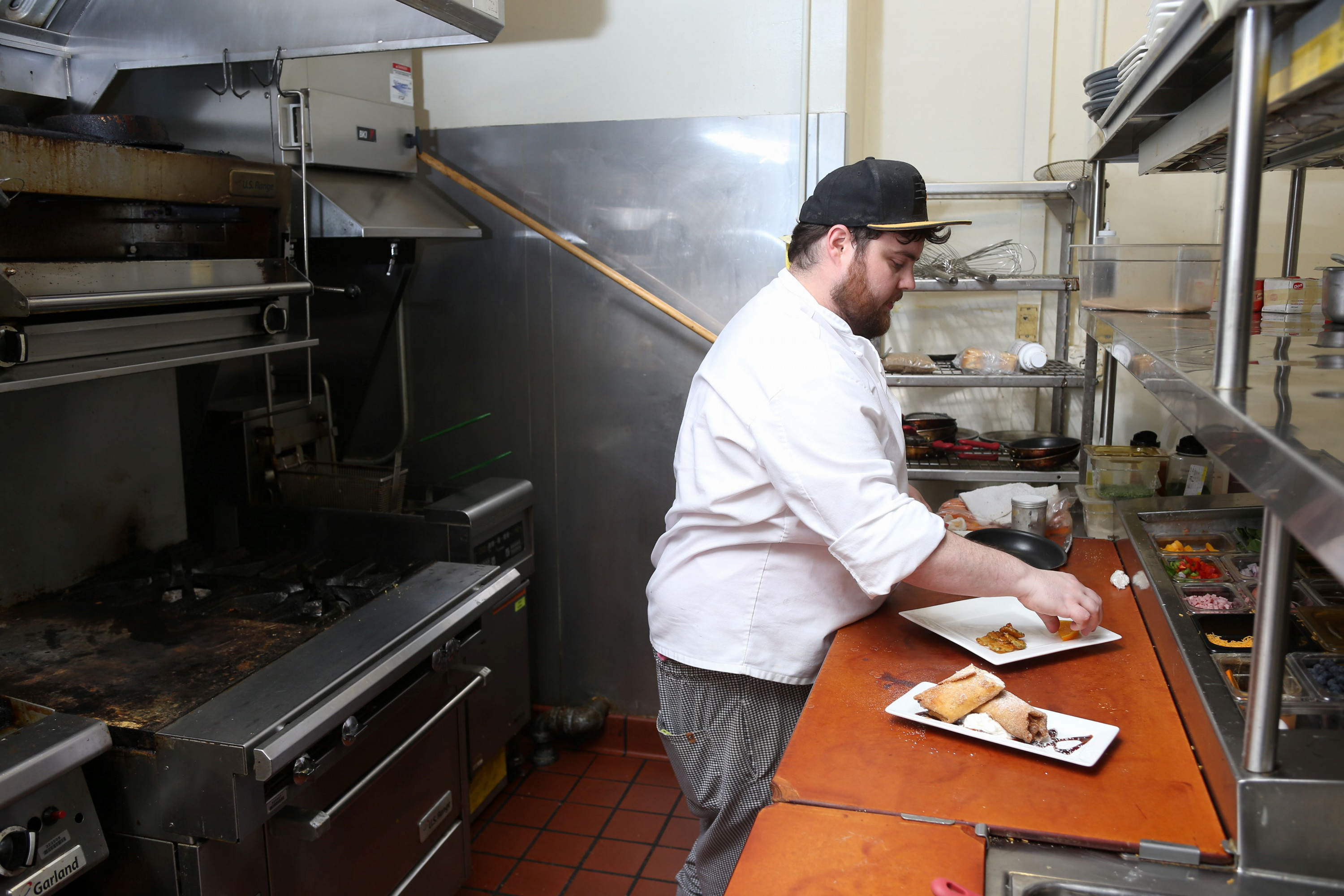 Man wearing a hat while preparing food in a restaurant kitchen