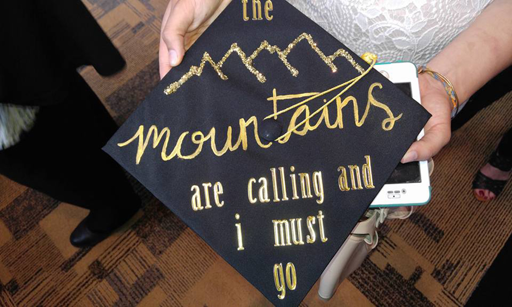 Graduation hat with painted text on top sharing "the mountains are calling and I must go".