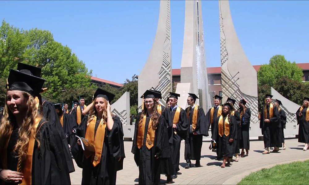 Graduates walking to commencement in cap and gown.