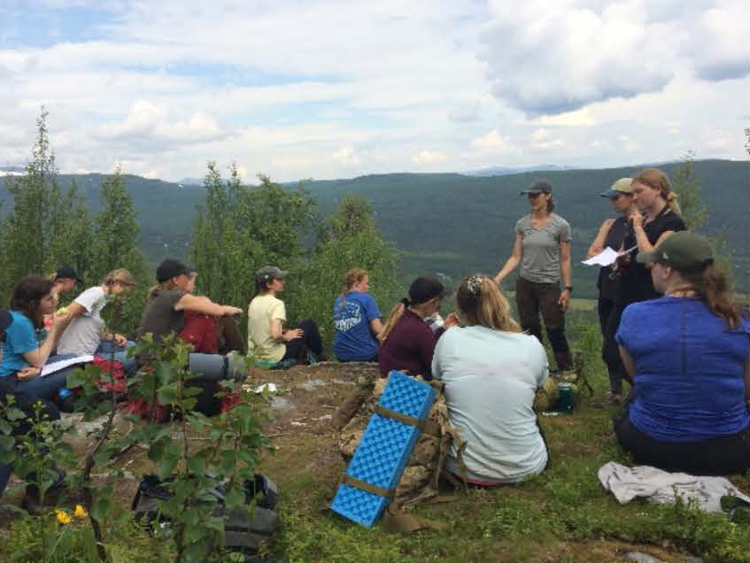 Study Abroad trip to Sweden, students sitting on hilltop with mountains in background.