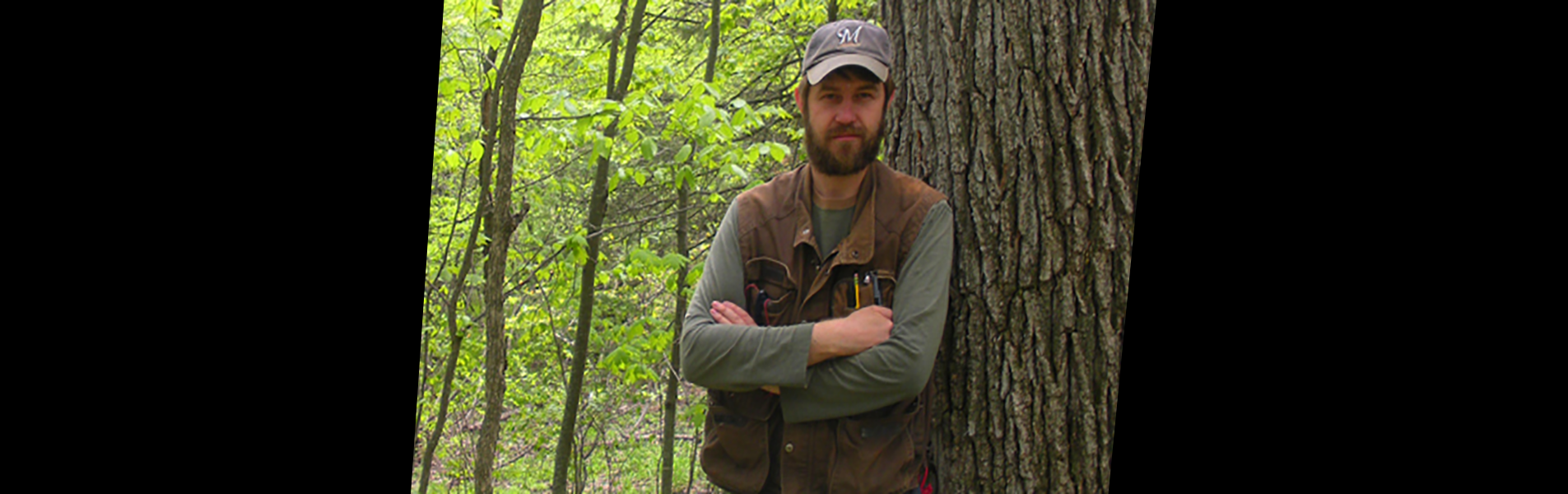 Andrew Meier, alumni, standing by tree in forest as he shares about his position with the US Army Corps of Engineers.