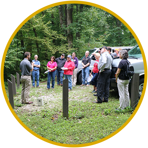 Natural Resources Educator talking with a group of professionals in woodlands.