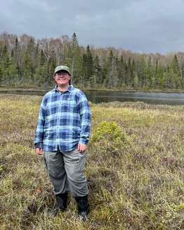 August South stands in a grassy field in front of a lake.