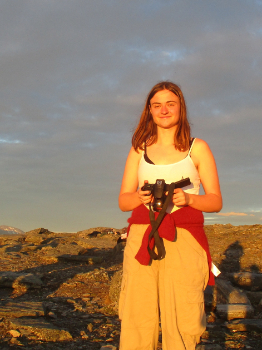 Brett Cox stands at sunset, holding a camera.