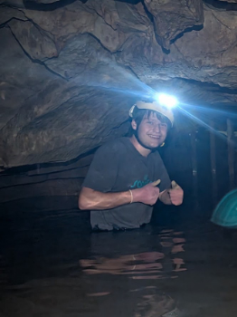 Collin Morris gives a double thumbs-up while standing in some water in a cave.
