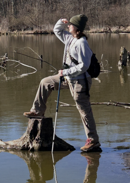 Jillian Kaufman puts one foot on a tree stump and looks off to the distance on the left.