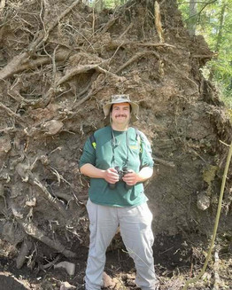 Karl Wing stands and smiles at the camera while holding a pair of binoculars.