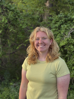 Katie Schouten stands in front of some bushes and smiles at the camera.