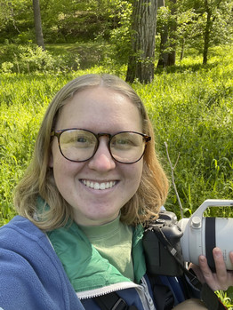 Kylee Thorson smiles, facing viewers, while holding a camera in one hand.