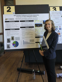Lydia Pultorak stands in front of a research poster in a suit.
