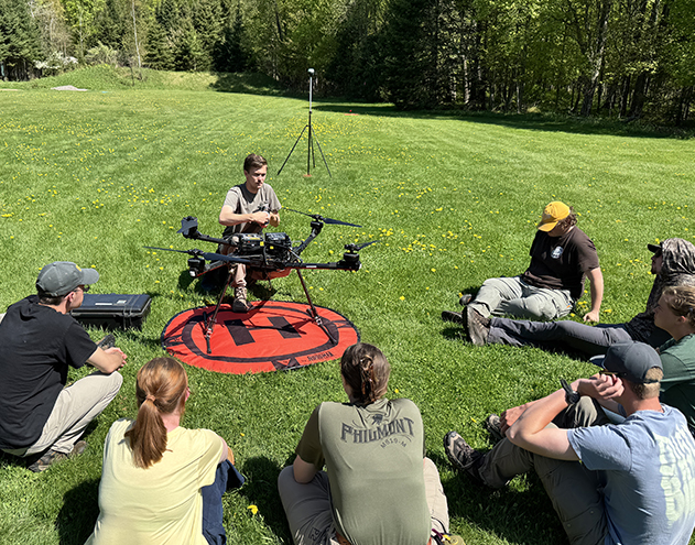 Instructor with students sitting on grass learning about drones.