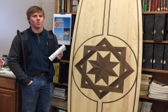 Student shows upright long table with brown trim inlays of a geometric and star shapes.